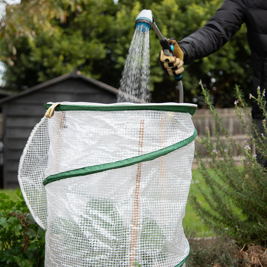 Person using a hose to water food plants in a home garden.